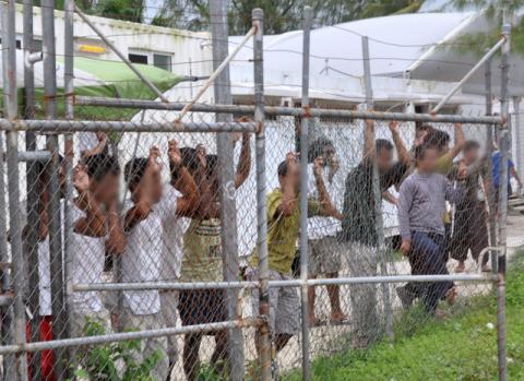 Asylum-seekers look through a fence at the Manus Island detention centre in Papua New Guinea March 21, 2014. PHOTO BY REUTERS/Eoin Blackwell