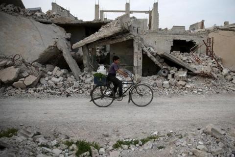 A boy rides a bicycle near rubble of damaged buildings in the rebel held besieged town of Douma, eastern Damascus suburb of Ghouta, Syria, March 19, 2016. PHOTO BY REUTERS/Bassam Khabieh