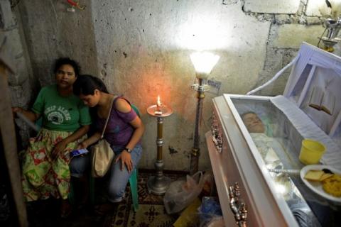 Rosalina Perez (L), 41, sits next to the coffin of her brother Benjamin Visda, who was shot by police during a drug investigation, inside their home in Manila, Philippines October 6, 2016. PHOTO BY REUTERS/Ezra Acayan