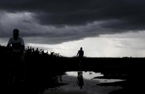 Storm clouds hover as cyclists pass a field of maize after late rains near Malawi's capital Lilongwe, February 1, 2016. PHOTO BY REUTERS/Mike Hutchings