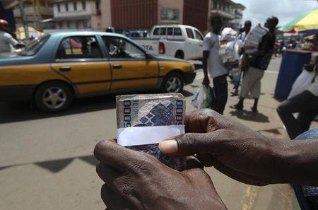A street money changer or 'Dollar Boy' holds a wad of local leone banknotes as he plies his trade on Siaka Stevens street in the heart of Sierra Leone's capital Freetown, June 9, 2011. PHOTO BY REUTERS/Simon Akam