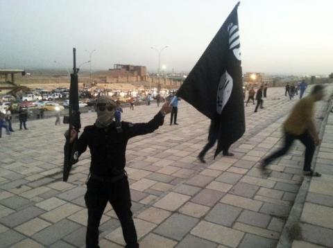 A fighter of the Islamic State of Iraq and the Levant (ISIL) holds an ISIL flag and a weapon on a street in the city of Mosul, June 23, 2014. PHOTO BY REUTERS/Stringer