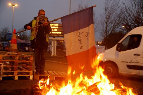 A protester wearing a yellow vest, the symbol of a French drivers' protest against higher diesel fuel prices, holds a flag near burning debris at the approach to the A2 Paris-Brussels Motorway, in Fontaine-Notre-Dame, France, December 4, 2018. PHOTO BY REUTERS/Pascal Rossignol