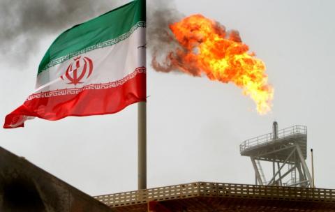 A gas flare on an oil production platform in the Soroush oil fields is seen alongside an Iranian flag in the Persian Gulf, Iran, July 25, 2005. PHOTO BY REUTERS/Raheb Homavandi