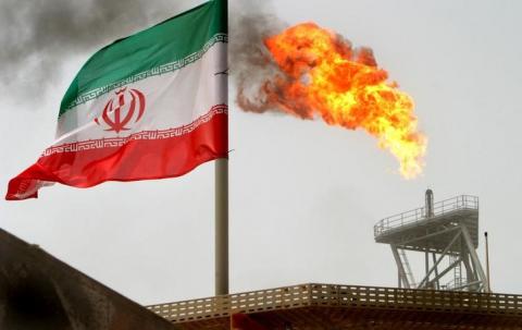Gas flare on an oil production platform in the Soroush oil fields is seen alongside an Iranian flag in the Gulf, July 25, 2005. PHOTO BY REUTERS/Raheb Homavandi