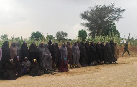 A man carrying a Boko Haram flag walks past a group of 82 Chibok girls, who were held captive for three years by Islamist militants, as the girls wait to be released in exchange for several militant commanders, near Kumshe, Nigeria, May 6, 2017. PHOTO BY REUTERS/Zanah Mustapha