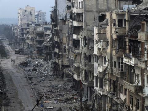 People stand on a street lined with damaged buildings in the besieged area of Homs
