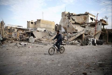 A young man rides bicycle near damaged houses in the besieged town of Douma, Eastern Ghouta, Damascus, Syria, February 20, 2018. PHOTO BY REUTERS/Bassam Khabieh