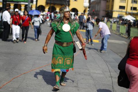 A man dressed as a native Inca walks as he watches the final ruling court session of a decades-old maritime dispute between Peru and Chile, on a television screen in the yard of the Government Palace in Lima