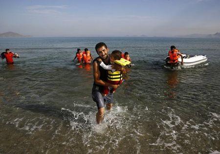 An Iranian migrant cries as while carrying his son after a small group of exhausted migrants from Iran arrived by paddling an engineless dinghy from the Turkish coast (seen in the background) at a beach on the Greek island of Kos, August 15, 2015. PHOTO BY REUTERS/Yannis Behrakis