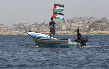 A Palestinian man riding a boat holds Palestinian flags during a protest against the Israeli blocking of a boat of foreign activists from reaching Gaza, at the Seaport of Gaza City, June 29, 2015. PHOTO BY REUTERS/Suhaib Salem