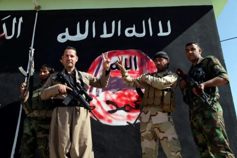 Kurdish Peshmerga fighters pose near a wall on which the black flag commonly used by Islamic State militants has been painted over, in the northern Iraqi town of Zumar, October 26, 2014, after having taken it from Islamic State. PHOTO BY REUTERS/Azad Lashkari