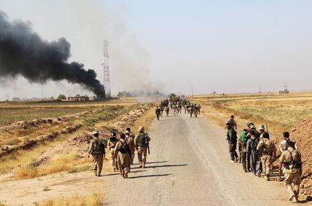 Kurdish Peshmerga fighters walk with their weapons as smoke rises from the site of clashes, south of Daquq, north of Baghdad, August 26, 2015. PHOTO BY REUTERS/Stringer