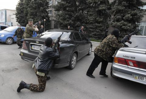 Pro-Russian armed men take cover behind cars near the local police headquarters in Luhansk, eastern Ukraine