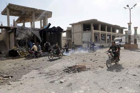 Residents ride motorcycles near a hole in the ground at a site hit by what activists said was an air strike by forces of Syria's President Bashar al-Assad, in Hesh village in the southern countryside of Idlib, Syria, September 27, 2015. PHOTO BY REUTERS/Khalil Ashawi