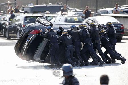 French riot police push an overturned car as striking French taxi drivers demonstrate at the Porte Maillot to block the traffic on the Paris ring road during a national protest against car-sharing service Uber, in Paris, June 25, 2015. PHOTO BY REUTERS/Charles Platiau