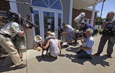 Sarah Madison (L) and her son Beckett, 3, are surrounded by media as they look at stuffed animals placed at the doorway of the River Bluff Dental clinic in protest against the killing of a famous lion in Zimbabwe, in Bloomington, Minnesota, July 29, 2015. PHOTO BY REUTERS/Eric Miller