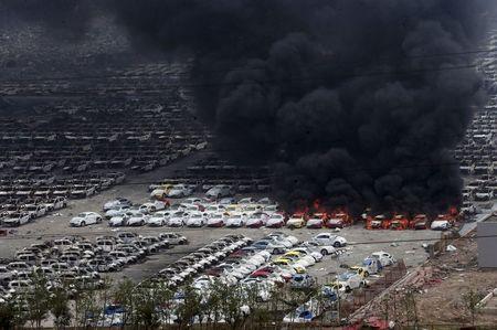 Smoke rises as damaged vehicles are seen burning near the site of Wednesday night's explosions, at Binhai new district in Tianjin, China, August 15, 2015. PHOTO BY REUTERS/Stringer