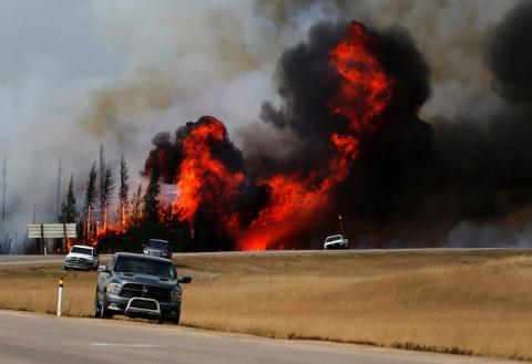 Smoke and flames from the wildfires erupt behind cars on the highway near Fort McMurray, Alberta, Canada, May 7, 2016. PHOTO BY REUTERS/Mark Blinch