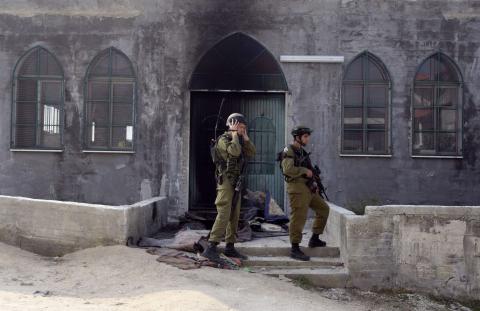 Israeli soldiers stand near the damaged door of a mosque, set ablaze by vandals, in the West Bank village of Urif, near Nablus