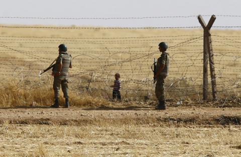 Turkish soldiers stand guard as a Syrian refugee boy waits behind the border fences to cross into Turkey on the Turkish-Syrian border, near the southeastern town of Akcakale in Sanliurfa province, Turkey, June 5, 2015. PHOTO BY REUTERS/Osman Orsal