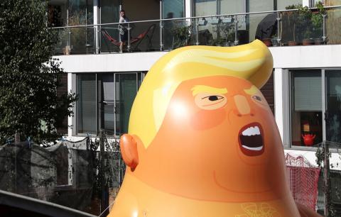 A man looks from his balcony as people inflate a helium filled Donald Trump blimp which they hope to deploy during The President of the United States' upcoming visit, in London, Britain, June 26, 2018. PHOTO BY REUTERS/Simon Dawson