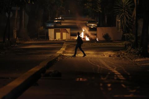 A woman walks past a burning barricade at Altamira Square in Caracas