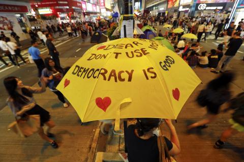 A woman sits under a yellow umbrella as pro-democracy protesters gather on a main street they occupy at Mongkok shopping district in Hong Kong, October 23, 2014. photo by REUTERS/Damir Sagolj