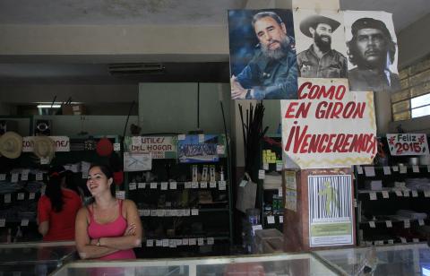 A woman stands near pictures of Cuban former president Fidel Castro (L), Cuban late rebel revolutionary Camilo Cienfuegos (C) and revolutionary hero Ernesto "Che" Guevara at a state store in Havana, December 27, 2014. PHOTO BY REUTERS/Stringer