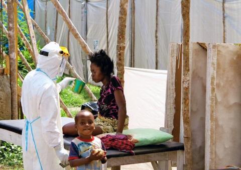 A health worker, wearing head-to-toe protective gear, offers water to a woman with Ebola, at a treatment centre for infected persons, as a young boy stands nearby in Kenema Government Hospital, in Kenema, Eastern Province, Sierra Leone, July 2014. PHOTO BY REUTERS/Jo Dunlop