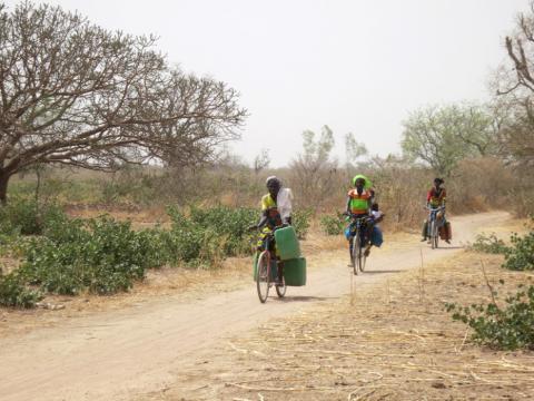Women cycle with water tins towards the village of Bagare, Passore province, northern Burkina Faso, March 30, 2016. PHOTO BY Thomson Reuters Foundation/Zoe Tabary