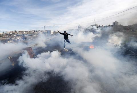 A Palestinian protester jumps as tear gas fired by Israeli soldiers rises during clashes in Jalazoun refugee camp near the West Bank city of Ramallah