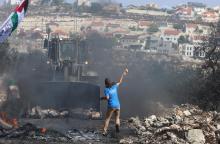 A Palestinian boy throws stones at an armored wheel loader of the Israeli Defense Forces (IDF) during clashes following a protest against the near-by Jewish settlement of Qadomem, in the West Bank village of Kofr Qadom near Nablus, October 17, 2014. PHOTO BY REUTERS/Abed Omar Qusini
