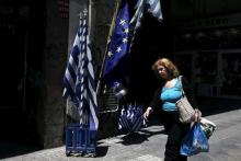 A woman carrying bags of goods makes her way past Greek national flags and European Union flags on display in Athens, May 25, 2015. PHOTO BY REUTERS/Alkis Konstantinidis