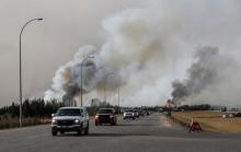 A group of evacuees in a convoy drive in front of smoke from the the wildfires near Fort McMurray, Alberta, Canada, May 6, 2016. PHOTO BY REUTERS/Mark Blinch