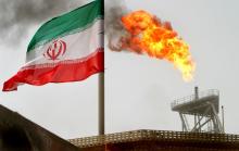 A gas flare on an oil production platform in the Soroush oil fields is seen alongside an Iranian flag in the Persian Gulf, Iran, July 25, 2005. PHOTO BY REUTERS/Raheb Homavandi