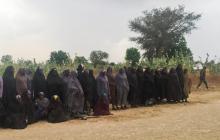 A man carrying a Boko Haram flag walks past a group of 82 Chibok girls, who were held captive for three years by Islamist militants, as the girls wait to be released in exchange for several militant commanders, near Kumshe, Nigeria, May 6, 2017. PHOTO BY REUTERS/Zanah Mustapha