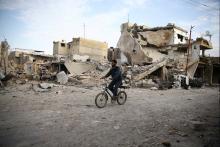 A young man rides bicycle near damaged houses in the besieged town of Douma, Eastern Ghouta, Damascus, Syria, February 20, 2018. PHOTO BY REUTERS/Bassam Khabieh