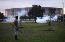 A native Brazilian stands in front of the Mane Garrincha soccer stadium as police use tear gas to impede a group of Indians from approaching it during a demonstration in Brasilia