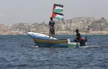 A Palestinian man riding a boat holds Palestinian flags during a protest against the Israeli blocking of a boat of foreign activists from reaching Gaza, at the Seaport of Gaza City, June 29, 2015. PHOTO BY REUTERS/Suhaib Salem