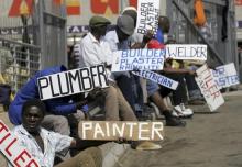 Men hold placards offering temporal employment services in Glenvista, south of Johannesburg, file. PHOTO BY REUTERS/Siphiwe Sibeko