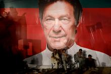 Labourers, who set up the venue, sit under a wall with a billboard displaying a photo of Imran Khan, chairman of the Pakistan Tehreek-e-Insaf (PTI), political party, as they listen to him during a campaign rally ahead of general elections in Karachi, Pakistan July 22, 2018. PHOTO BY REUTERS/Akhtar Soomro