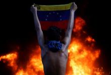 A protester holds a national flag as a bank branch, housed in the magistracy of the Supreme Court of Justice, burns during a rally against Venezuela's President Nicolas Maduro, in Caracas, Venezuela, June 12, 2017. PHOTO BY REUTERS/Carlos Garcia Rawlins