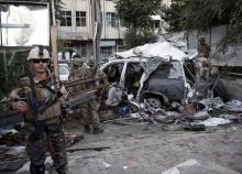Afghan security personnel (L) keeps watch next to a damaged car belonging to foreigners, after a bomb blast in Kabul, Afghanistan, August 22, 2015. PHOTO BY REUTERS/Ahmad Masood