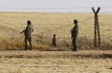 Turkish soldiers stand guard as a Syrian refugee boy waits behind the border fences to cross into Turkey on the Turkish-Syrian border, near the southeastern town of Akcakale in Sanliurfa province, Turkey, June 5, 2015. PHOTO BY REUTERS/Osman Orsal