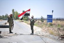 A member of forces loyal to Syria's President Bashar al-Assad holds the national flag as another one gestures in al-Ghariya al-Gharbiya in Deraa province, Syria in this handout released on June 30, 2018. PHOTO BY SANA/Handout via REUTERS