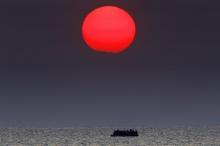 A red sun is over a dinghy overcrowded with Syrian refugees drifting in the Aegean sea between Turkey and Greece after its motor broke down off the Greek island of Kos, August 11, 2015. PHOTO BY REUTERS/Yannis Behrakis
