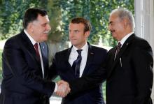 French President Emmanuel Macron stands between Libyan Prime Minister Fayez al-Sarraj (L), and General Khalifa Haftar (R), commander in the Libyan National Army (LNA), who shake hands after talks over a political deal to help end Libya's crisis in La Celle-Saint-Cloud near Paris, France, July 25, 2017. PHOTO BY REUTERS/Philippe Wojazer
