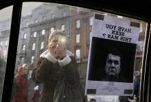 A woman takes photos of a "Wanted" notice for fugitive Ukrainian President Victor Yanukovich, plastered on the window of a car used as a barricade, near Kiev's Independent Square