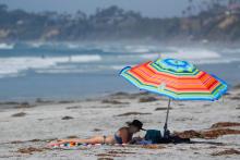 A women keeps in the shade of her umbrella as she tries to beat the heat at Cardiff State beach in Encinitas, California, U.S. July 6, 2018. PHOTO BY REUTERS/Mike Blake